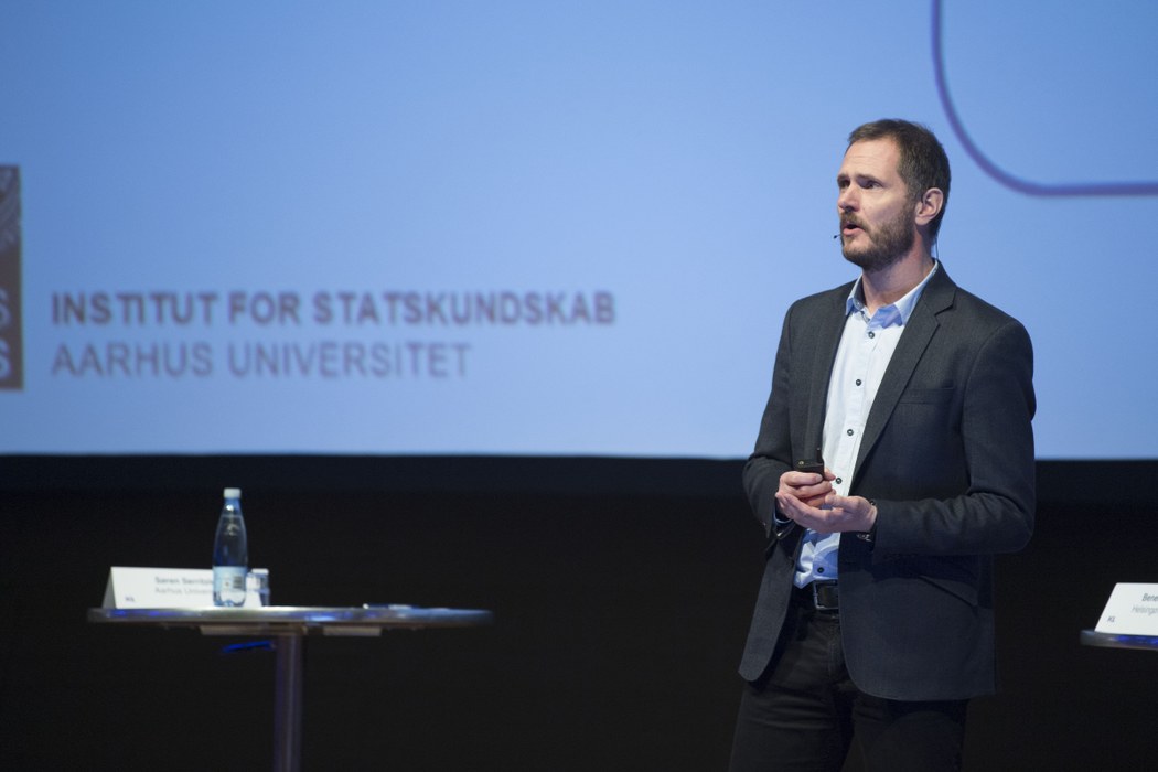 Foto af Søren Serritzlew på en scene med et slide i baggrunden, hvor der står Institut for Statskundskab, Aarhus Universitet