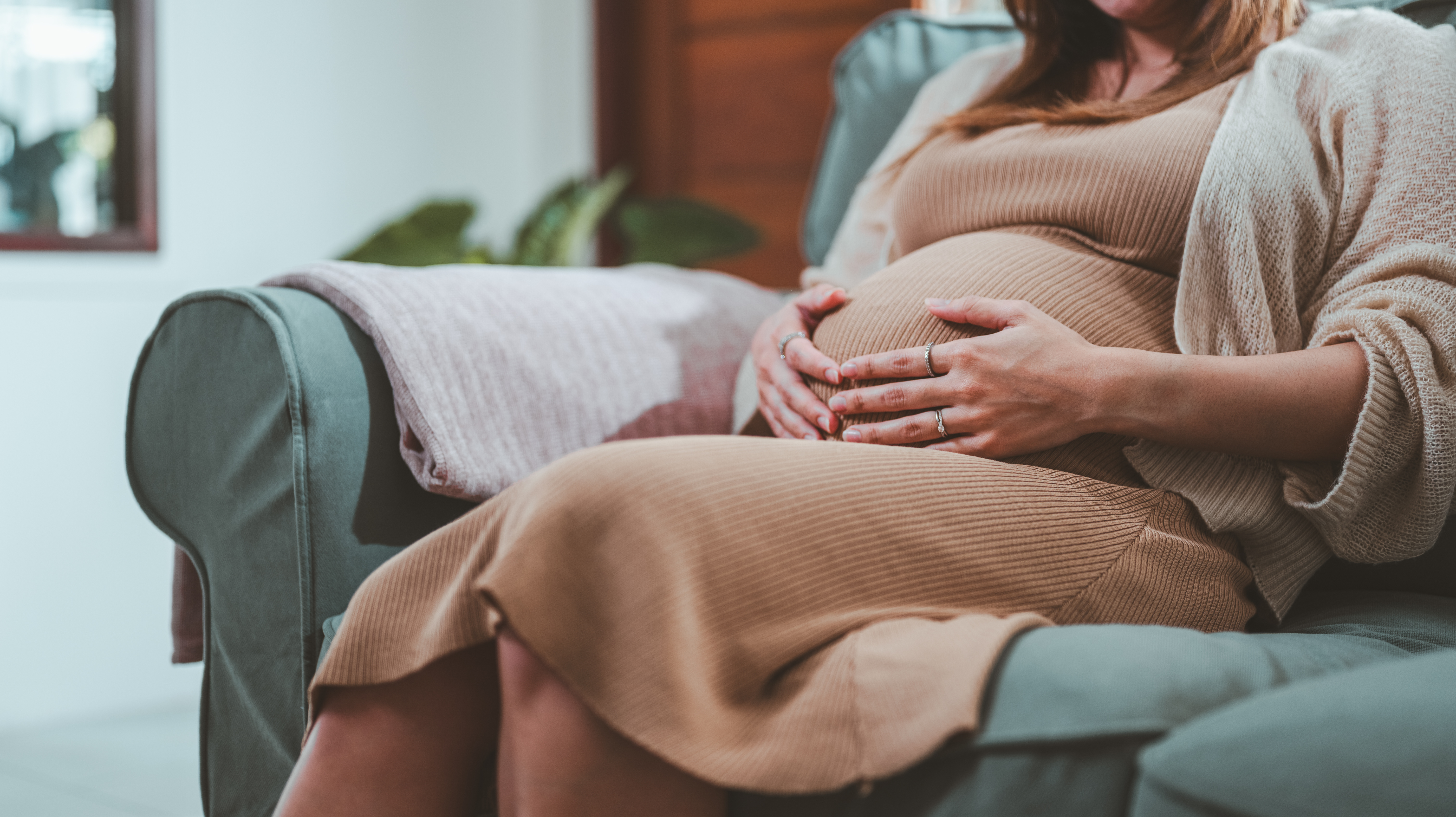 Gravid kvinde sidder i stol og holder hænderne på maven. 