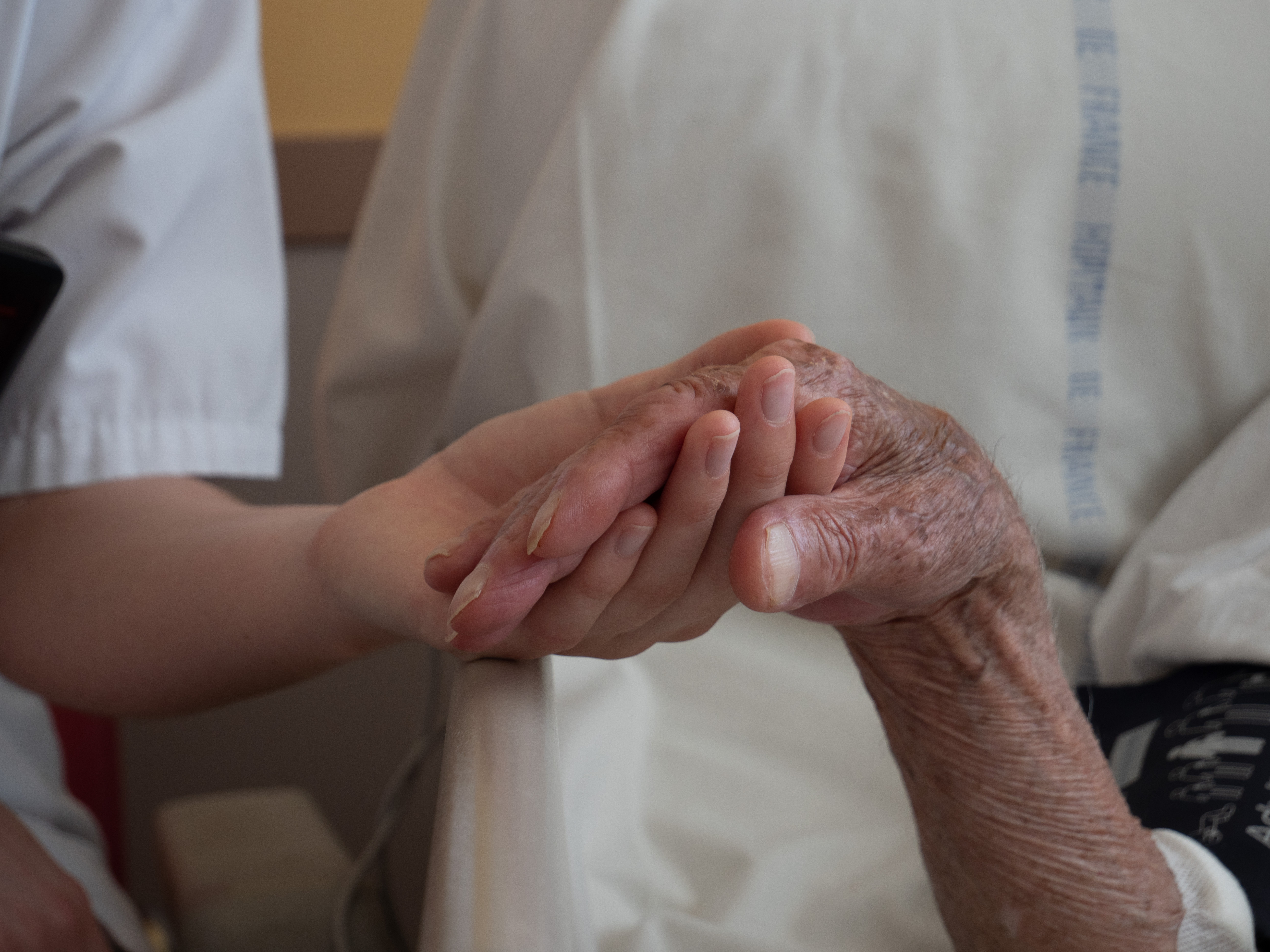 Et nærbillede af to hænder, der holder i hånden. Den ene hånd tilhører en sygeplejerske eller plejer, mens den anden hånd er en ældre patient.