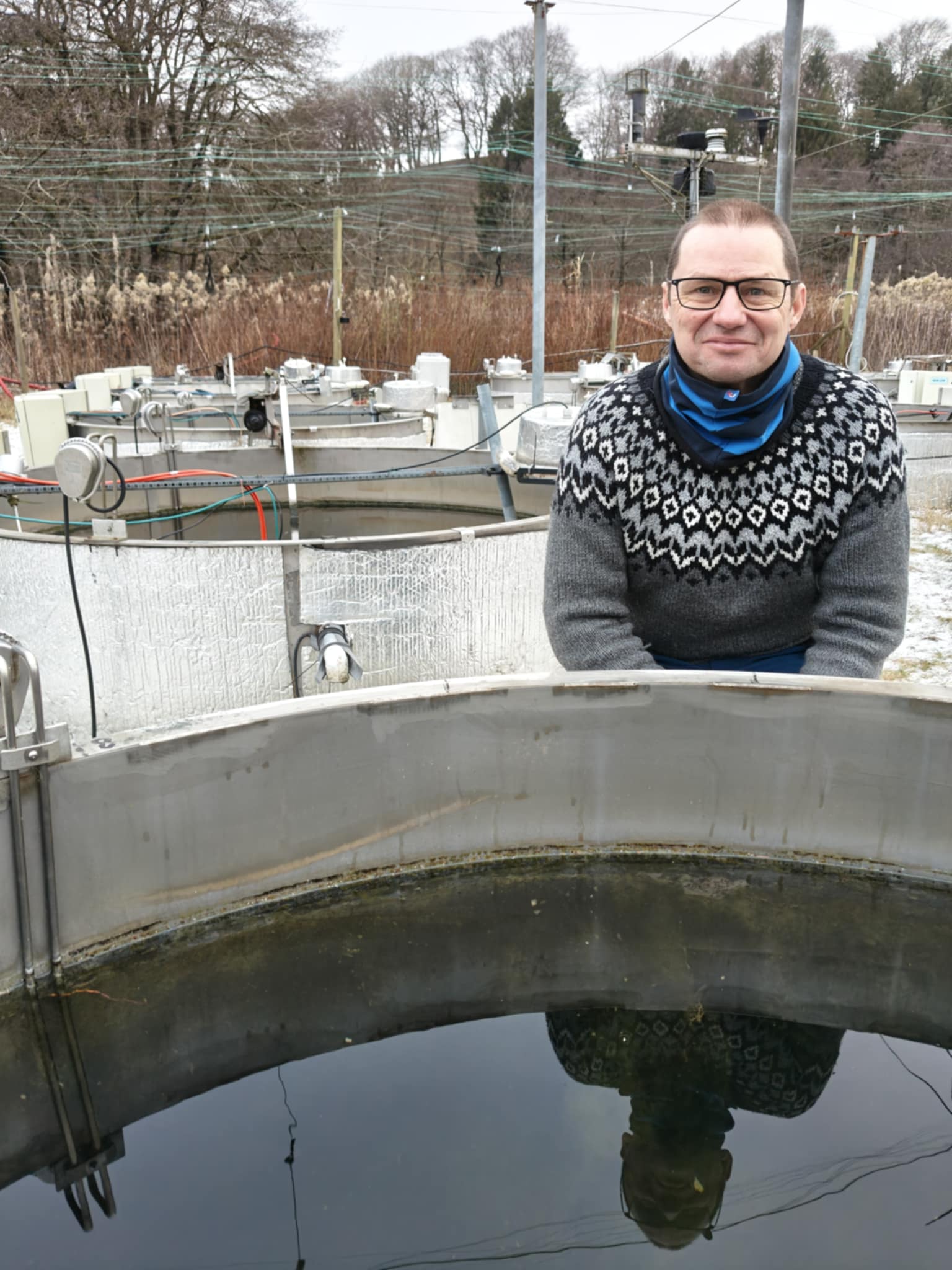 Foto af Tom Davidsen i striktrøje med sne i baggrunden og foran ham et stort kar med vand 