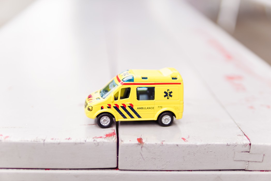 Et nærbillede af en gul legetøjs ambulance stående på en slidt grå bænk
