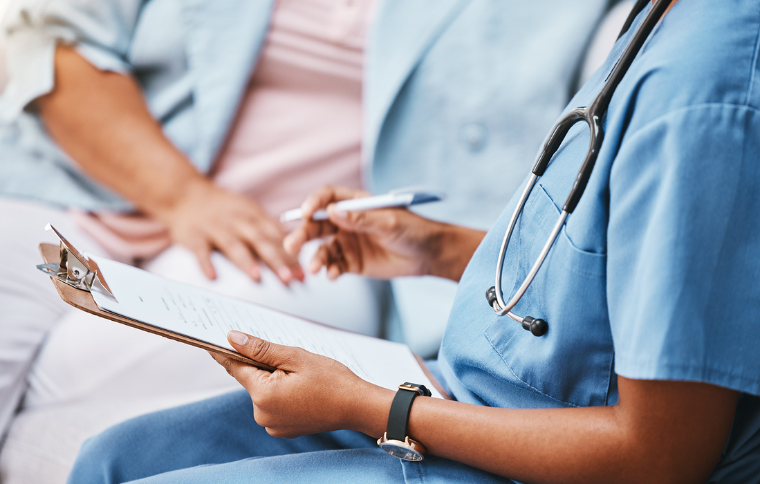 En læge der har en kuglepind i den en hånd og et papir i den anden imens hun snakker til patienten