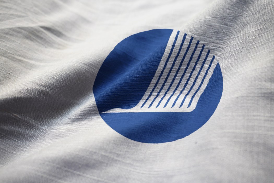 Logo af hvid stiliseret fugl på en blå cirkel. Dette på et hvidt stykke stof